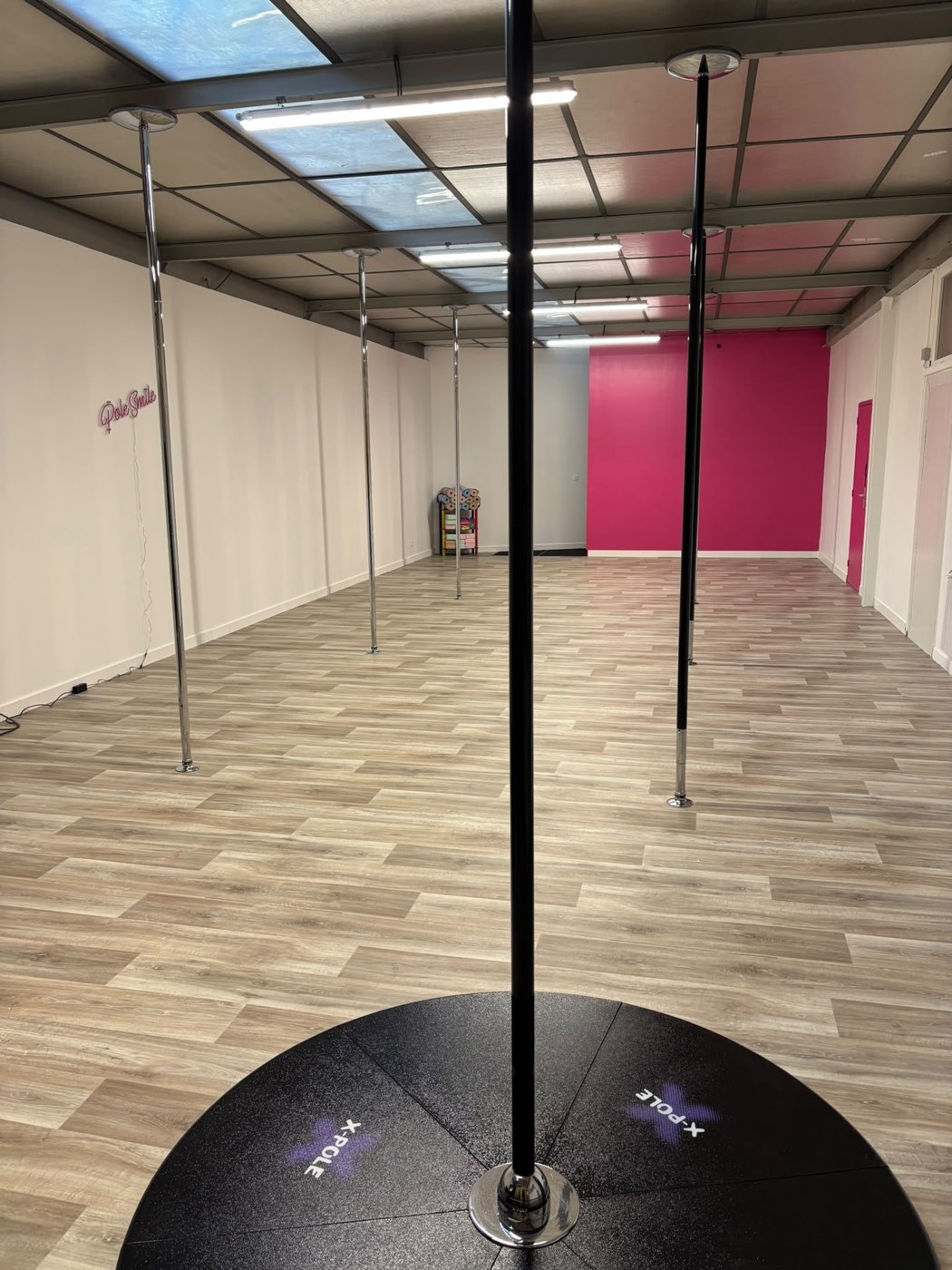 Le mur rose et le néon Pole Smile, avec une barre X-Pole sur scène