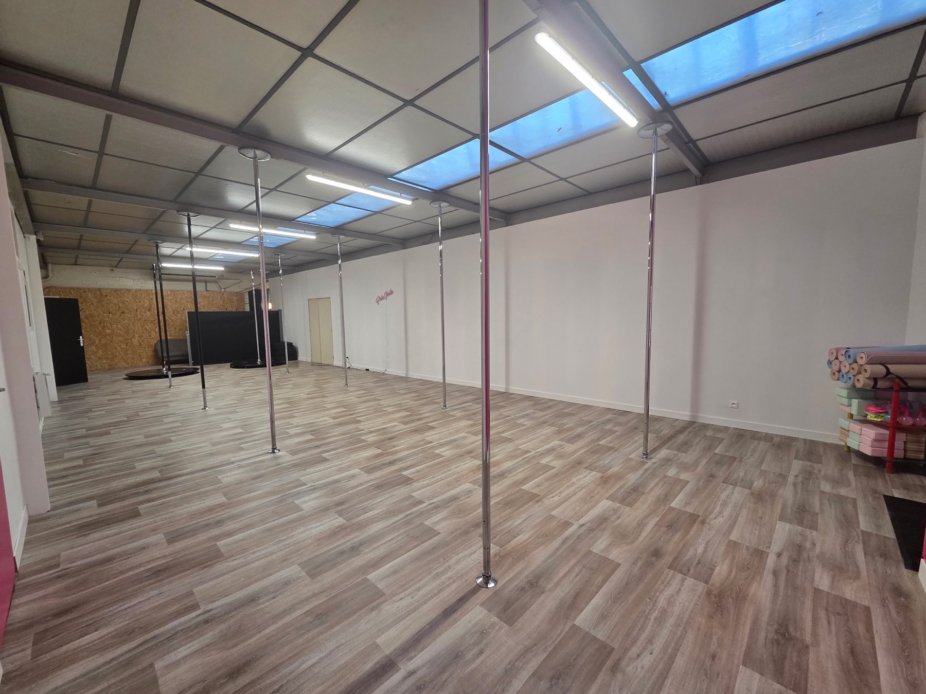 La salle de Pole Smile : grand parquet clair, barres de pole dance et lumière naturelle